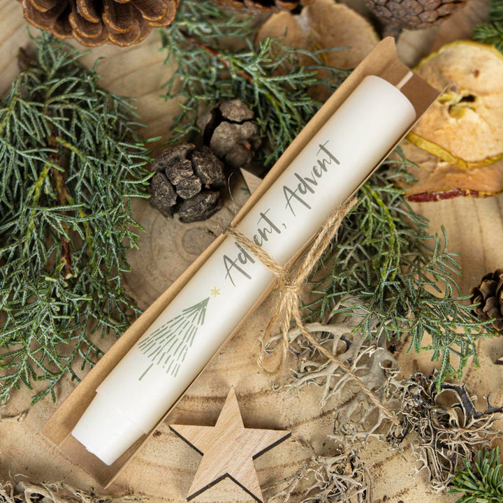 Cremefarbene Stabkerze Advent neben einer Geschenkverpackung aus Karton in winterlicher Dekoration