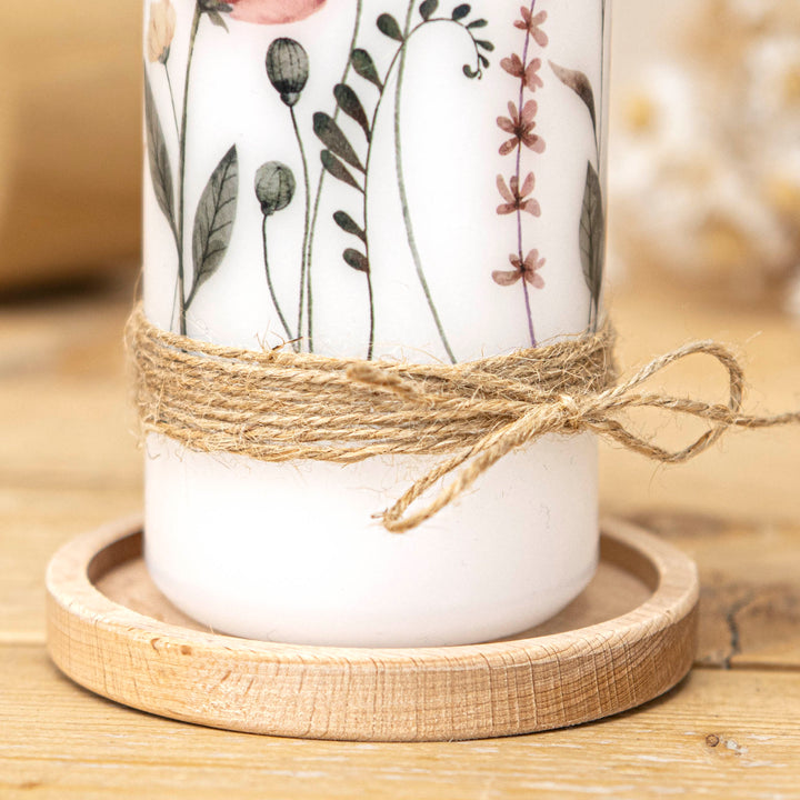 Untere Kerzenhälfte mit Wildblumen-Motiv und geknoteter Bastkordel auf einem Holzteller